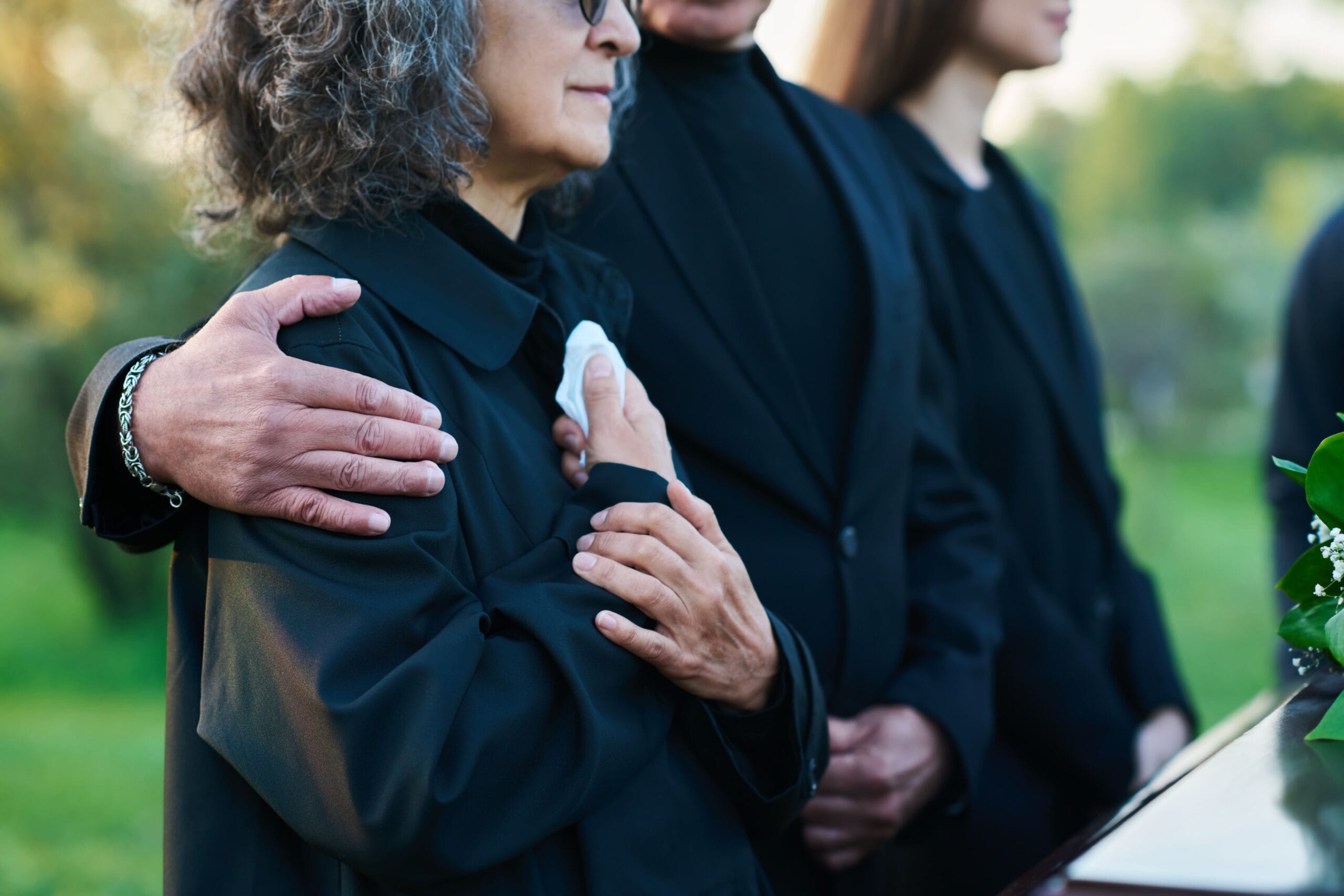 Persona vestida con ropa oscura y discreta asistiendo a un funeral en un cementerio